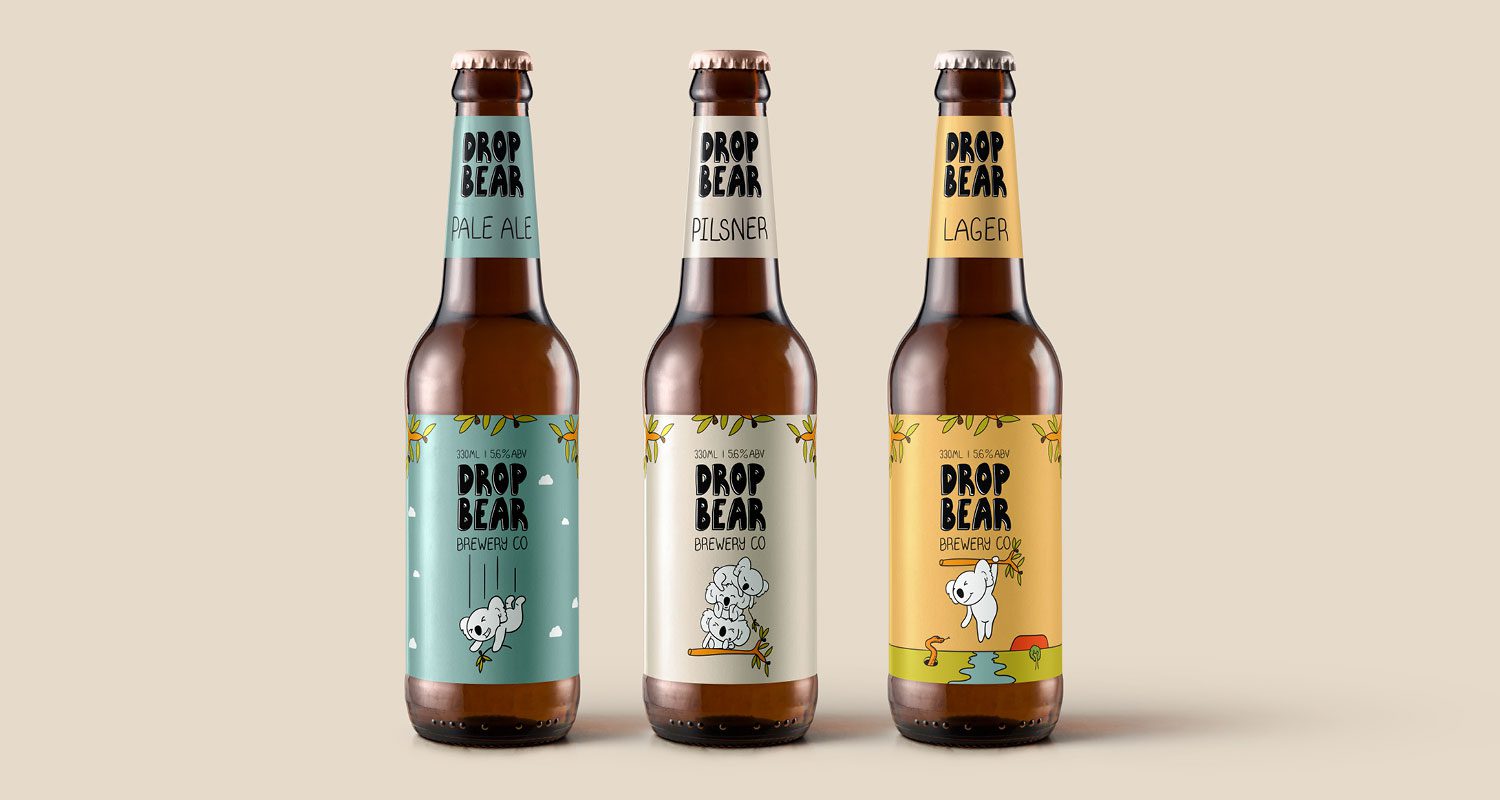 Photograph of three bottles of beer featuring the Drop Bear brand identity on their labels. The bottles are isolated on a neutral background. The labels use an Australian-inspired color palette and feature simple, outlined illustrations of animated koalas.