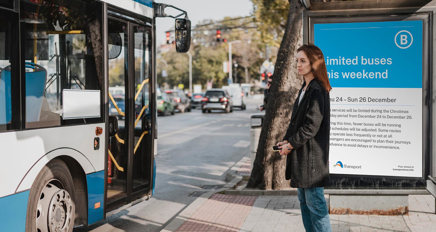 Photograph of a Transport for NSW operational template displayed on a bus station poster, with a woman waiting at the bus stop for a blue bus in the background.
