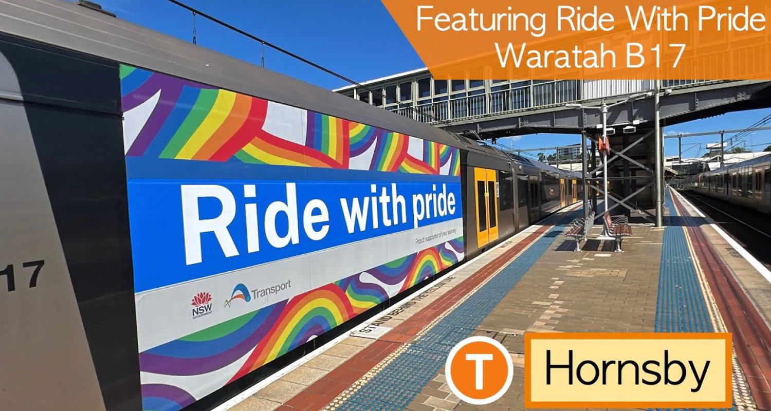 Photograph of a pride-themed message displayed on a train wrap at a train station reading “Ride with Pride,” with a train and commuters in the background, promoting LGBTQ+ visibility.