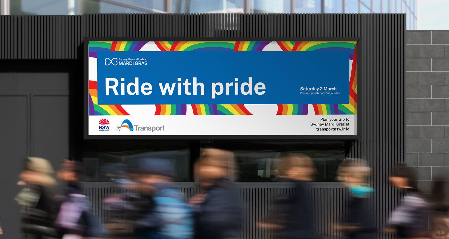 Photograph of a public transport scene featuring a pride-themed digital screen, diverse passengers walking, and a train station backdrop, promoting inclusivity and the “Ride with Pride” campaign by Transport for NSW.